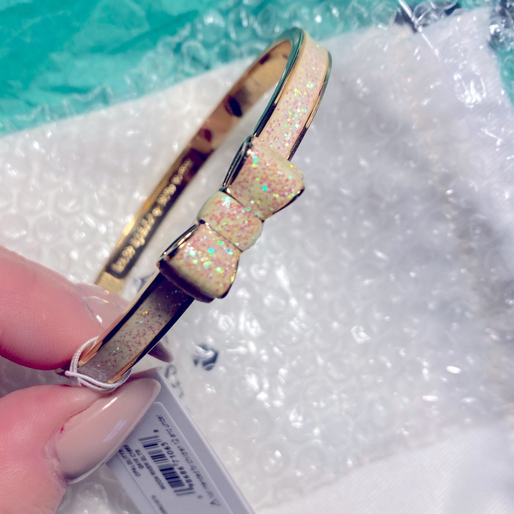 Kate Spade Take a Bow bangle bracelet. Gold tone w/ white iridescent main color.